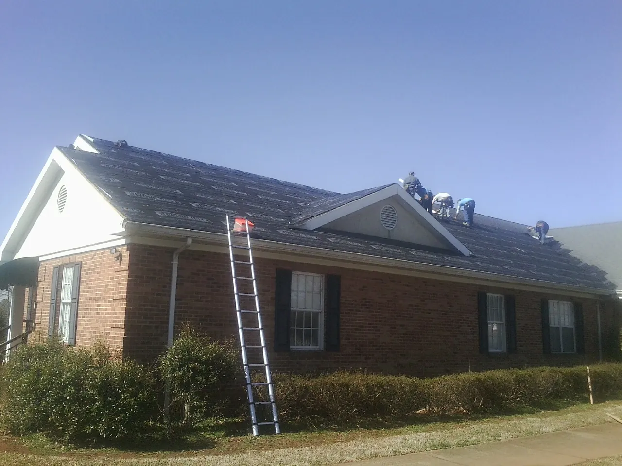 Crew tearing shingles off a brick ranch roof with a ladder set — Emergency Roof Repair work by our crew in Stantonsburg