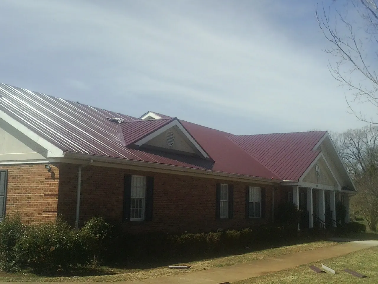 Red metal roof with gabled entries on a long brick building, from a Hail Damage Roof Repair job in Stantonsburg