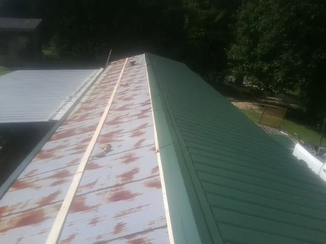 Old rusted panels beside newly installed green metal roofing — Wind Damage Roof Repair by Roofing Brothers in Stantonsburg