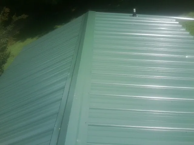 New green metal panels meeting at the ridge of a roof — Flat Roof Repair work by our crew in Stantonsburg
